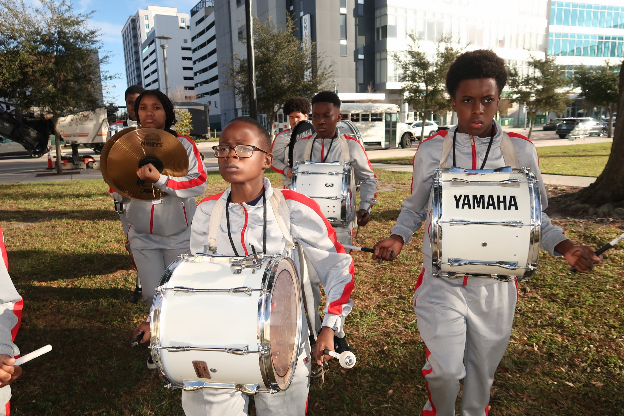 children in a drum line dressing in band uniforms marching down a field